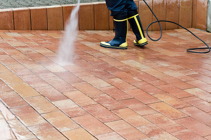 Person spraying water onto brick pavers